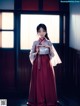 A woman in a red and white kimono standing in front of a window.