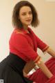 A woman in a red shirt and black skirt sitting on a chair.