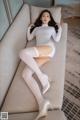 A woman in a white bodysuit and high heels laying on a couch.