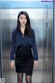 A woman in a blue shirt and black skirt standing in an elevator.