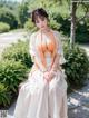 A woman in a white and orange dress sitting on a bench.