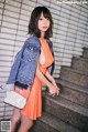 A woman in an orange dress and a denim jacket posing for a picture.