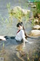 A woman in a white shirt and black skirt is sitting in the water.