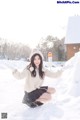 A woman in a white sweater and black skirt crouching in the snow.