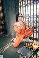 A woman in an orange jumpsuit sitting on the ground next to a yellow tool box.