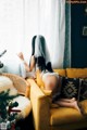 A woman sitting on a yellow couch in front of a window.