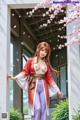 A woman in traditional attire stands by an open door with cherry blossoms and petals around her.