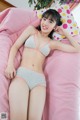 A woman laying on a pink bed wearing a gray and pink bikini.
