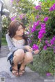 A woman kneeling down next to a bush of purple flowers.