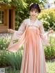 A young girl in a pink hanbok standing in a garden.