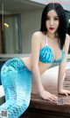 A woman in a blue bikini sitting on a wooden bench.