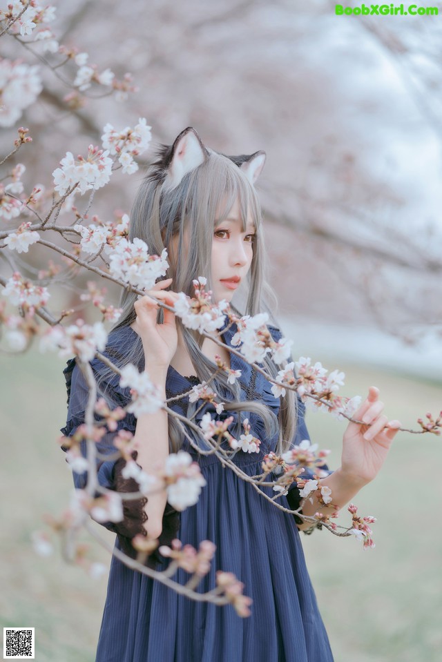 A woman in a blue dress holding a branch of a tree.