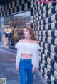 A woman standing in front of a wall wearing a white top and jeans.