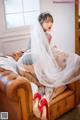 A woman in a wedding dress sitting on a brown couch.