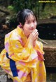 A woman in a yellow kimono sitting on a rock.