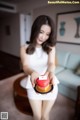 A woman in a white dress holding a red heart shaped cake.