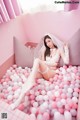 A woman in a white lingerie sitting in a pink ball pit.