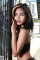 A woman in a black bra top leaning against a fence.